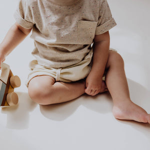 Baby wearing a stylish sprinkle knit T-shirt with a pocket, sitting on the floor and playing with a toy.