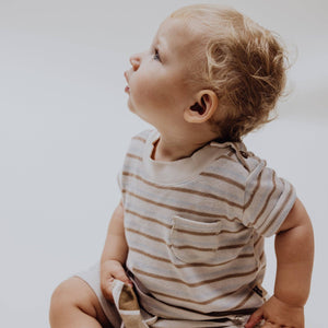 Baby wearing a multi-striped organic cotton T-shirt, looking curiously, showcasing soft fabric and practical shoulder buttons.