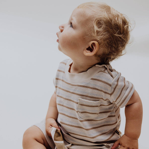 Baby wearing a multi-striped organic cotton T-shirt, looking curiously, showcasing soft fabric and practical shoulder buttons.