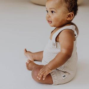 Cute baby in a soft knitted organic cotton romper with adjustable straps sitting gracefully.