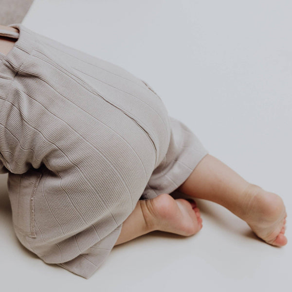 Baby wearing Latzhose in Rippenstrick Stone, showcasing soft fabric and flexible fit for summer adventures.