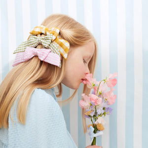 Mädchen mit Grosse Gingham Haarschleifen in Minze, Senfgelb und Korallenrosa, riecht an einem Strauß Blumen. Perfektes Accessoire für Kinder ab 4 Jahren.