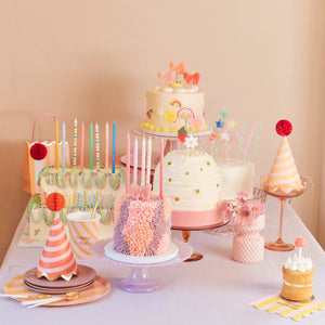 Birthday cakes and cupcakes adorned with colorful candles and hats, creating a festive celebration atmosphere.