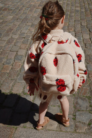 Child wearing Jody Teddyjacke with ladybug design and backpack on cobblestone path, showcasing cozy and stylish outerwear.