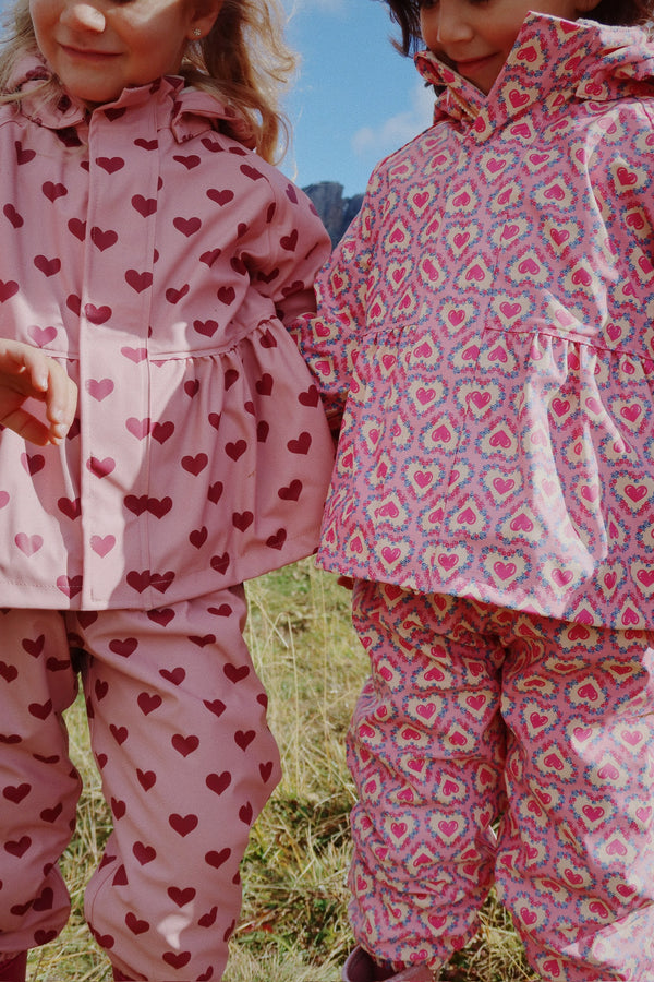 Two children wearing colorful rain suits with heart patterns, enjoying the outdoors in wet weather.