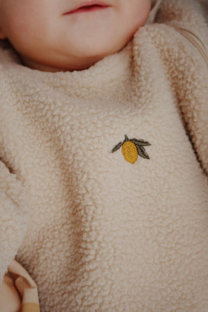 Baby in a cozy Oxford Tan fleece onesie featuring a cute lemon embroidery detail.
