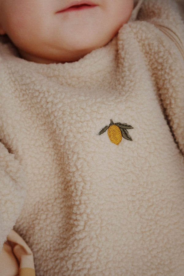 Baby in a cozy Oxford Tan fleece onesie featuring a cute lemon embroidery detail.