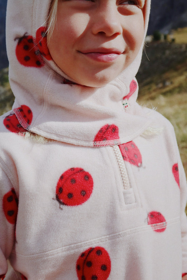 Girl smiling in a cozy Tavi fleece-sweatshirt featuring a playful ladybug design, perfect for warmth on chilly days.
