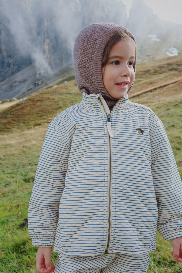 Child wearing a warm striped Thermojacke Stripe Bluie jacket in a scenic outdoor setting.