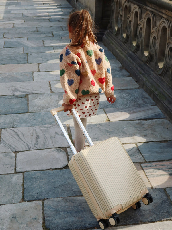 Child pulling Reisekoffer Tea Stripe suitcase on a stone pathway, wearing a heart-patterned sweater.