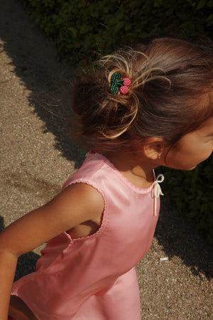 Young girl in a pink dress wearing a cherry hair clip outdoors, showcasing playful hairstyle.