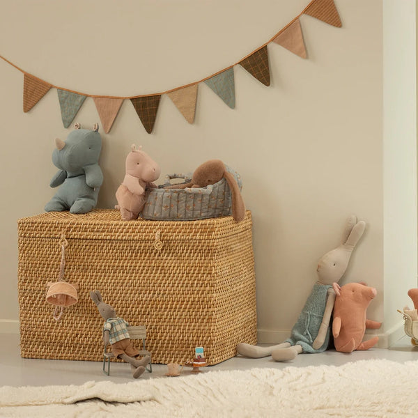 Colorful plush toys including rhinos and rabbits arranged around a woven basket in a cozy children's room.